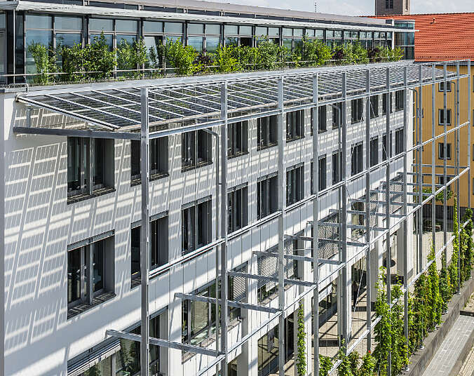 Gebäude mit Fassadenbegrünung an Seilen und Gerüst mit Photovoltaikanlage