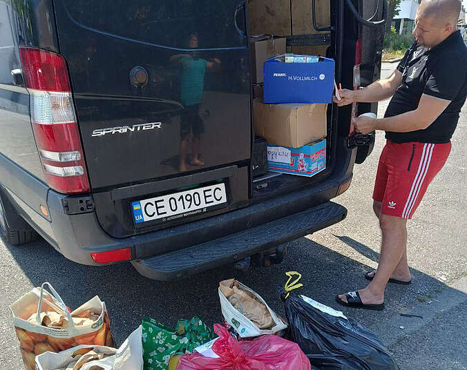 Ein Mann lädt Taschen und Pakete mit Sachspenden in einen blauen Kleinbus ein.